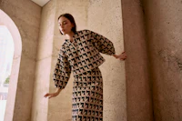 a woman is leaning against a wall in a patterned skirt